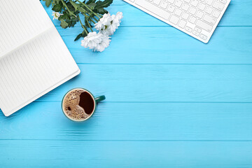 Cup of coffee, notebook, keyboard and flowers on color wooden background