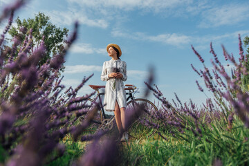 Young woman with retro bicycle and lavender bouquet on violet flowers field background