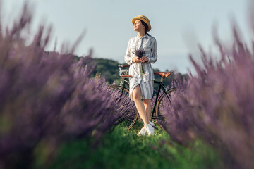 Young woman with retro bicycle and lavender bouquet on violet flowers field background