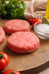Wooden board with raw cutlets made of fresh forcemeat on table, closeup