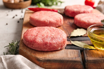 Wooden board with raw cutlets made of fresh forcemeat on table, closeup