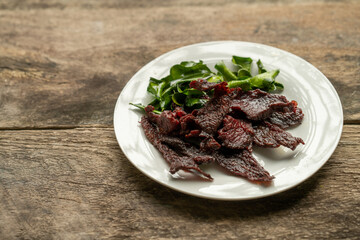 Fried sun dried beef in white plate on wooden table.