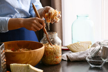 Obraz na płótnie Canvas Woman putting tasty sauerkraut into glass jar on table in kitchen, closeup