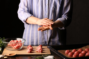 Woman preparing tasty cutlets made of fresh forcemeat on dark background, closeup
