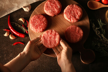 Woman preparing tasty cutlets made of fresh forcemeat on dark background, closeup