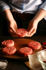 Woman preparing tasty cutlets made of fresh forcemeat on dark background, closeup