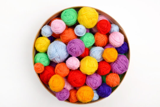 A lot of colorful,woolen balls of knitted yarn in a round cardboard box on a white background.The concept of handmade work, needlework and the sale of thread.Top view.Flatlаy.Rainbow layout.Copyspace.