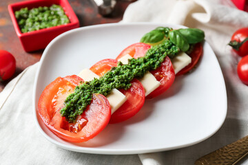 Plate with caprese salad and pesto sauce on table