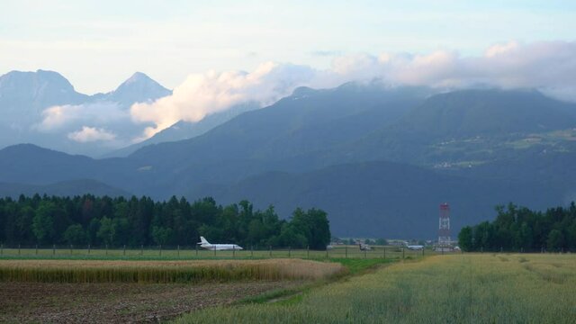 Luxury private jet taxiing on the runway, Ljubljana airport, Slovenia. Airplane on the runway. Wheat field in the foreground, Alps mountains in the distance. Right pan, real time