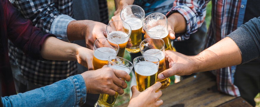 Cropped shot of people holding beer glasses celebrating in the summer camping party outdoor. Friends clinking bottle of beer during camping outdoor