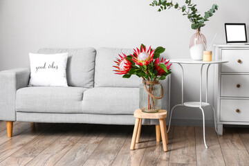 Table with protea flowers and sofa in interior of room