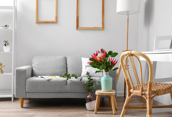 Table with protea flowers and sofa in interior of room