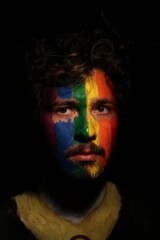 Portrait of young man face painted as lgbtq progress pride flag with direct lighting on face with dark black copy space empty background *5