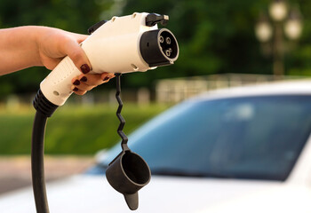 A female hand takes the charging cable of an electric vehicle. The driver with a cable for charging an electric car in the background of a car. Green alternative energy concept