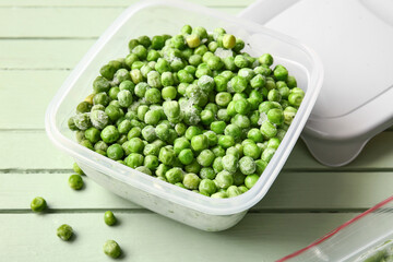Container with frozen green peas on color wooden background