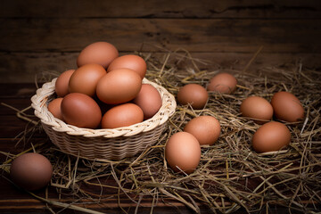 Chicken eggs in baskets with nest of straw on wooden table, wood background.