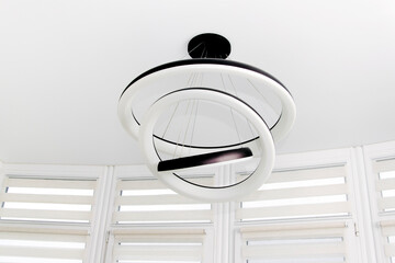 Modern round white chandelier with led lamps hanging on the ceiling in the apartment