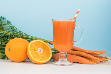 Orange and carrot smoothie, carrots and oranges on a white table.