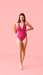 Fototapeta na wymiar Beautiful young woman in swimsuit and with cocktail on color background