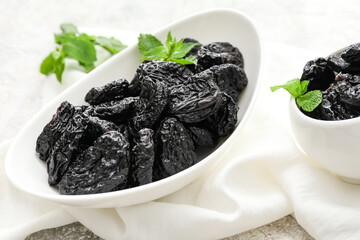 Plate with tasty prunes on light background