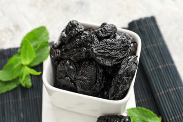 Bowl with tasty prunes on light background, closeup