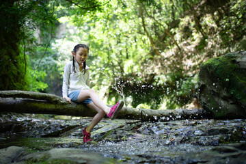 倒木に座って川遊びをする少女