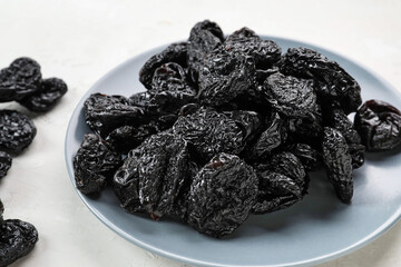 Plate with tasty prunes on light background, closeup