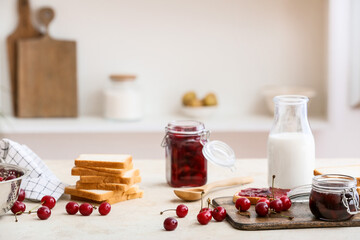 Jar with tasty cherry jam, bread and bottle of milk on table in kitchen