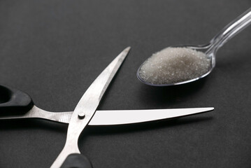 Scissors and a white sugar in a transparent spoon on black background.