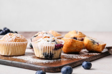 Board with tasty blueberry muffins on light background, closeup