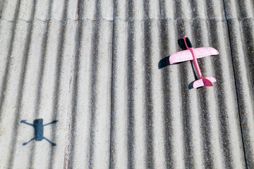 A pink foam airplane and the shadow of a drone next to it, on a slate roof