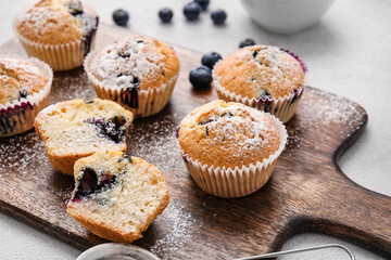 Board with tasty blueberry muffins on light background, closeup