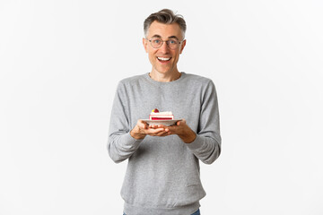 Portrait of happy handsome middle-aged man, wearing glasses and gray sweater, holding cake and...