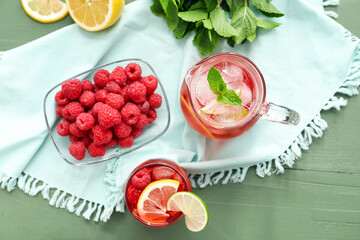 Glasses of tasty lemonade and bowl with raspberry on color wooden background