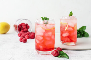 Glasses with tasty raspberry lemonade on light background