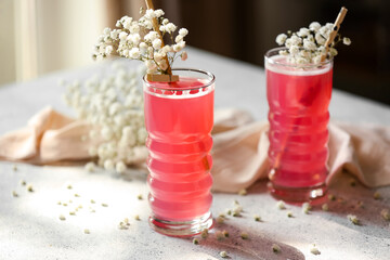 Glasses with tasty cocktail and beautiful gypsophila flowers on light background