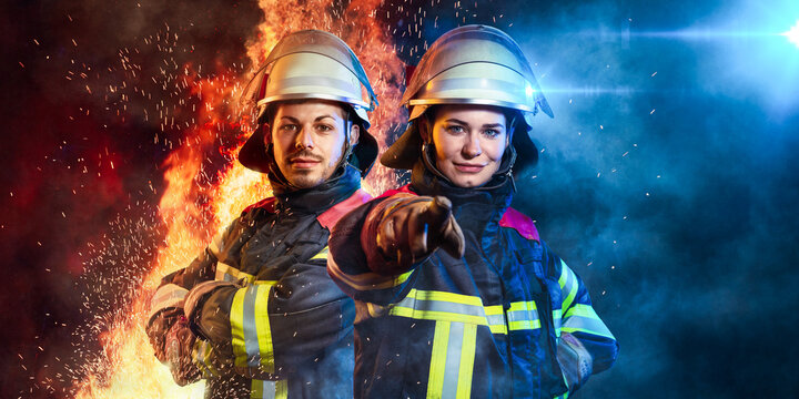 Ein Feuerwehrmann und eine Feuerwehrfrau stehen zusammen vor Feuer und Blaulicht