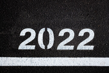 Numbers for the year 2022 written in white on the black asphalt of a polluted road.