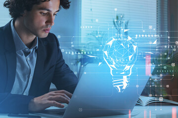 Businessman browsing internet via laptop at office workplace to find new ideas for start up. Blue digital hologram of light bulb. Concept of creativity and brainstorming