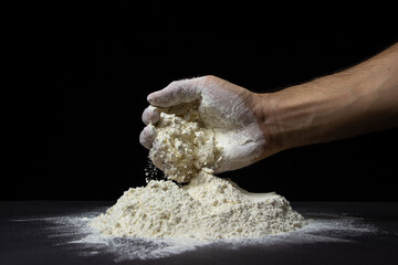 Hand takes flour from a heap of flour on a black background. Flour of the highest grade on a dark background