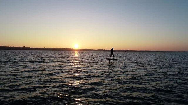 E Foil Sunset boating on the water. Paddleboard, stand-up surfing on electric foil. Aerial drone shot at sunrise. Luxury lifestyle, superyacht water toys.