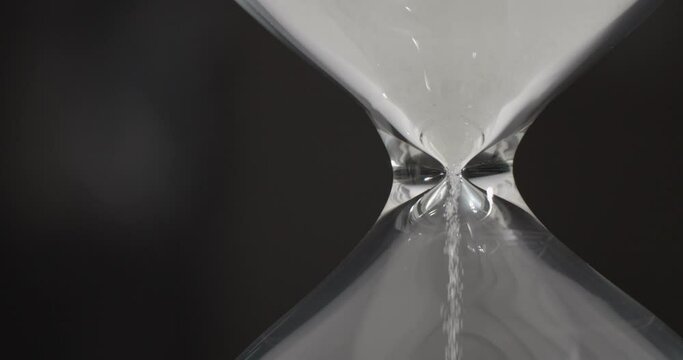 Hourglass or sandglass : Closeup of white sand falling down through a narrow neck in a sand clock or sand timer. Indicating passing of time. Each hourglass measures and has specific duration of time.