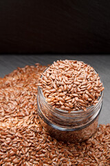 Flax seeds in a glass jar on a dark background with place for text vertical