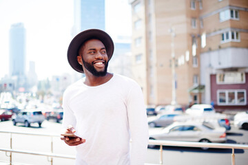 Cheerful male tourist dressed in white wear with copy space area for brand advertising smiling at city street, happy African American travel model in blank clothes holding cellphone device