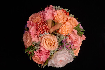 round bouquet of orange roses and other flowers on black background