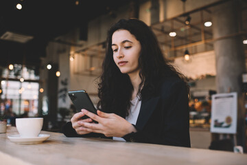 Obraz na płótnie Canvas Calm woman surfing smartphone and enjoying hot coffee in cafe
