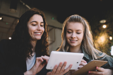 Joyful female colleagues browsing tablet and taking notes in workspace