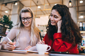Smiling women writing notes in planner while sitting in cafe