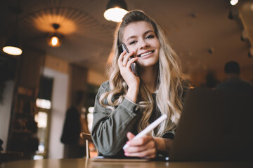 Female talking on phone while working on laptop in cafe