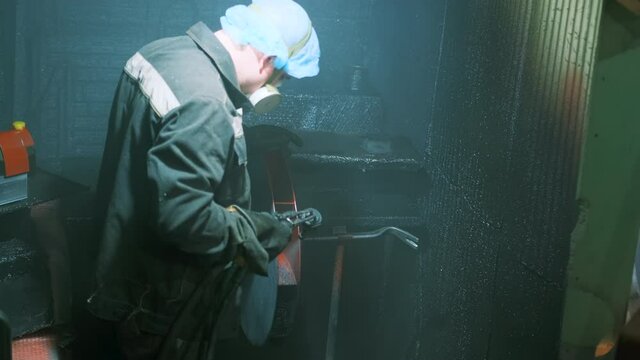 A man in a factory sprays polyurethane on a part. Spraying polyurethane on metal to protect against corrosion and abrasion. Coating with two-component cold curing polyurethanes for industrial products